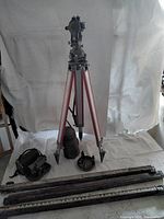 Overall view of lot on white backdrop showing transit on tripod, second transit and cases, rods and base plate