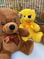 Close-up of two large teddy bears, one brown with a brown bow and one yellow with a yellow bow, showing facial details and soft plush material.