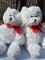 Two white small plush teddy bears with curly fur and red ribbons.