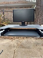 Ergotron standing desk converter showing wide gray work surface with monitor on top and keyboard tray below.