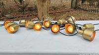 Set of 10 gold metal hanging lights arranged on a table, showing the whole string with black cable.