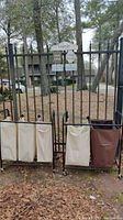 Laundry sorter with four fabric bags hanging on black metal frame, placed outdoors on grass near a black iron fence