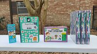 Front view of all four educational learning items arranged side by side outdoors: Brain Quest Math card set, magnetic bulletin board, Let's Learn Sign Language flash cards, and colorful binder with pages.
