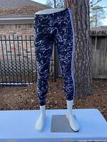 Front view of the male lower body mannequin with black marble-patterned leggings and white side stripes displayed outdoors on a metallic base.