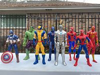 Photo of all 8 figurines including Captain America, Hulk, Wolverine, two Spider-Man, two Iron Man, and Flash figurines displayed outside on a white surface.