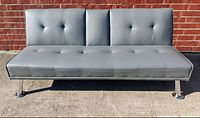 Front view of the gray futon sofa bed showing button-tufted upholstery and chrome legs.