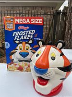 Photo showing the Tony The Tiger cookie jar next to a Kellogg's Frosted Flakes cereal box, illustrating size and design.