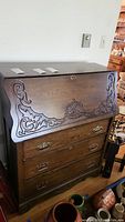 Front view of the antique oak secretary desk showing carved fold-down front and four drawers below with brass hardware.