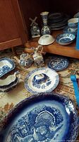 Full view of assorted blue and white china including teapots, trays, plates, and condiment dispensers arranged on floor showing chip damage.