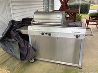 Full front view of the stainless steel Straubelstone Steelman gas grill with lid closed and side towel bar. Grill cover partially visible draped over side.