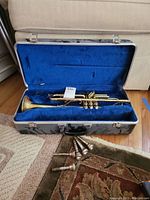 King brass trumpet with case on floor, mouthpieces arranged in front on carpet.
