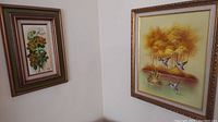 View of two framed paintings hanging in a corner. One depicts yellow flowers and the other shows three birds near a pond with trees.