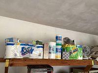 Photo of shelf showing Scott 1000 toilet paper, Clorox disinfecting wipes, Bounty paper towels, tissue boxes, and two tabletop fans.