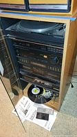 Full view of Pioneer stereo system components housed in wooden cabinet with glass front door, including turntable, receiver, CD player, dual cassette deck, and equalizer controls. Vinyl record on cabinet base with cables and remote controls.