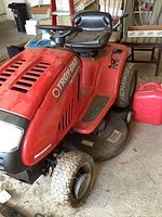 Side view of red Troy-Bilt Bronco riding mower showing flat front left tire, black seat and steering wheel