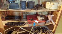Wide view on shelving showing vintage flat irons, tins, shoe forms, cake saver tin, metal trays, and paper mache dog figure.
