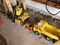 Four vintage Tonka construction vehicles arranged on a concrete floor showing their overall condition and size relative to each other.