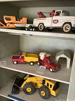 Multiple items across three shelves: orange loader, green semi, tow truck, dump truck, cement mixer, barn and loader.
