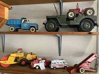Overview of multiple vintage toy vehicles on wooden shelves showing overall lot composition and condition.