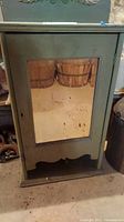 Front view of painted wooden wall cabinet with inset mirror showing scuffs and stains