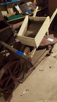 Photo showing both wheelbarrows stacked, highlighting white wooden wheelbarrow on top and reddish-brown on bottom with visible wear and age marks.