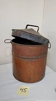 View of antique copper pot with lid partially opened showing the inside and exterior handles.