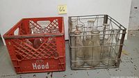 Red Hood plastic milk crate and wire metal crate filled with clear glass milk bottles against white background