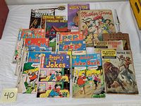 Front view of vintage comic and children's books laid out on a white cloth showing variety of titles including Archie, Reggie's Joke Book, Pep, Treasure Chest, Classics Illustrated, Jack and Jill, Mother Goose, and Henny Penny.