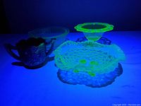 Three piece uranium glass set glowing under UV light showing distinct yellow-green fluorescence typical of uranium glass.