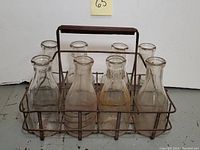 Front and side views of vintage metal milk bottle crate with handle and 8 glass milk bottles inside, showing condition of rust and wear on crate and bottles.