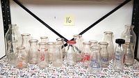 Full view of 17 vintage milk bottles on floral fabric surface with different logos and shapes, showing variety in the collection.