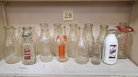 Front view of 15 assorted vintage milk bottles on shelf, showing various sizes and logo prints including Houlton Farms Dairy and Harlow's Milk