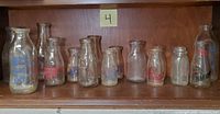 Shelf with 11 various vintage milk bottles including Federal Dairy, Round House Dairy, and Harlow's brands