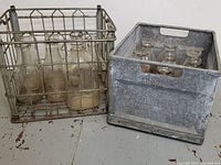 Two vintage milk crates side by side filled with glass milk bottles, showing weathered and rusted metal crates and clear vintage glass bottles.