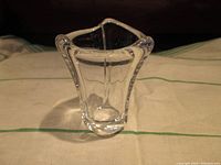 Small clear crystal vase with scalloped flared opening and thick base, photographed from front angle.