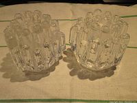 Pair of clear textured glass candle holders on cloth background, showing top and side views to highlight design and condition.