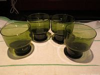 Four olive green stemmed wine glasses displayed on a white cloth with a green stripe.