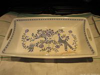 Full view of rectangular serving tray showing integrated handles and painted design with floral and human motifs in blue, purple, and green on cream background.