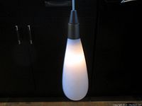Pendant light illuminated showing tapered frosted glass shade and metal cap.