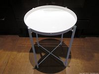 White metal side table with removable round tray top. The legs have a foldable X-frame design. The top tray has a minor dent on the edge and two leg caps are missing.