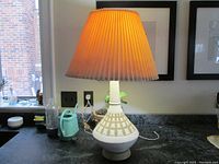 Full view of the Mid Century ceramic lamp lit up on a countertop, showing its shape and pleated fabric shade.