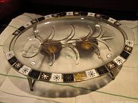Clear oval glass carving tray with embossed abstract design and decals around the edge, shown standing on integrated feet.