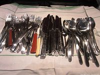 Wide photo showing the full set of forks, knives, and spoons arranged neatly on a cloth background
