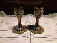 Pair of ornate metal candle holders with matching scalloped trays, showing white stone decorations.