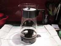 Front view of the Pyrex coffee carafe on the warmer showing the clear glass with vertical ribbed egg and dart design and black handle and lid.