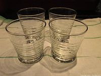 Front view of four clear ribbed rocks glasses, showing their cylindrical shape and ribbed texture
