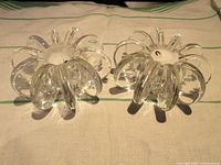 Pair of clear crystal taper candleholders resembling petals radiating from center, placed on cloth.