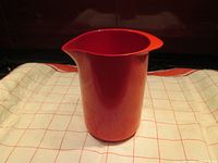 Red plastic Rosti pitcher on white and red checkered cloth, showing integrated handle and spout.