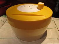 Side view of large yellow and white Triumph salad spinner with lid and knob on top.