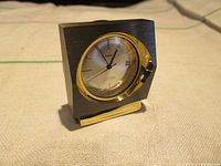 Front angled view of the Volvo branded travel clock with brushed metal body and gold bezel.